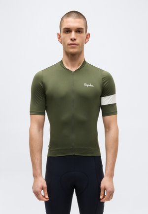 Moški model nosi kratko rokav kolesarsko majico olivno zelene barve z belo črto na rokavu in črne oblazinjene kolesarske hlače, stoji na enobarvni podlagi.