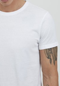 Hvid bomulds t-shirt med rund hals og korte ærmer, der har rullede manchetter. Stoffet ser glat ud med en let tekstur.