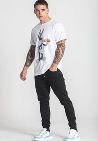 Bílá tričko s černou grafikou kresleného králíka. V kombinaci s černými slim-fit kalhotami a teniskami s modrými akcenty. Neformální streetwearový styl.