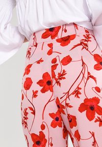 Roze bloemenbroek met een patroon van rode bloemen en groene stelen, met een aansluitend ontwerp en een hoge tailleband voor een getailleerde uitstraling.