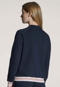 Marineblauwe sweatshirt met een ribgebreide kraag en zoom, voorzien van horizontale strepen in pastelkleuren aan de onderkant. Zacht materiaal, comfortabele pasvorm.