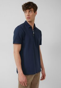 Granatowa koszulka polo z bawełny, z zamkiem błyskawicznym przy kołnierzu. Krótkie rękawy i prosty dół z bocznymi rozcięciami dla większej swobody ruchów.