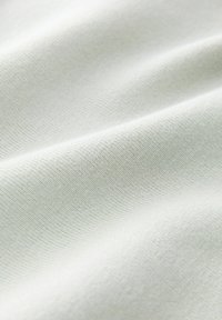 Tissu blanc lisse avec une texture côtelée fine et des plis délicats créant des ombres douces.