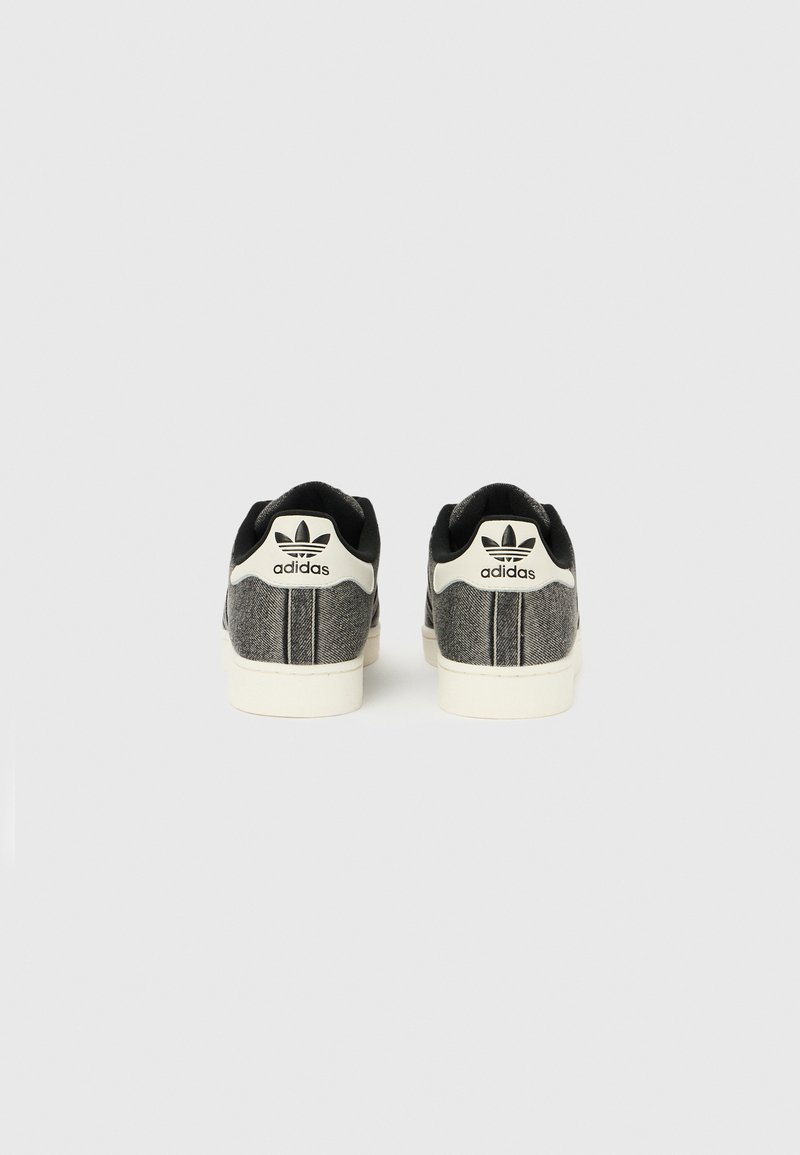 Paire de baskets Adidas en denim noir avec semelles blanches et languettes de talon affichant le logo Adidas sur un fond blanc uni.