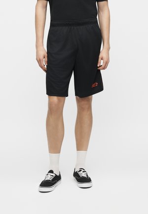 Mand iført sorte netshorts med elastisk taljebånd, sort t-shirt, hvide ankelsokker og sorte lave sneakers på hvid baggrund.