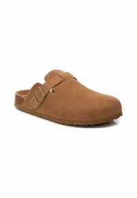 Zueco de ante marrón con una correa con hebilla, punta redondeada y suela texturizada estilo corcho. Diseño minimalista sin patrones visibles.
