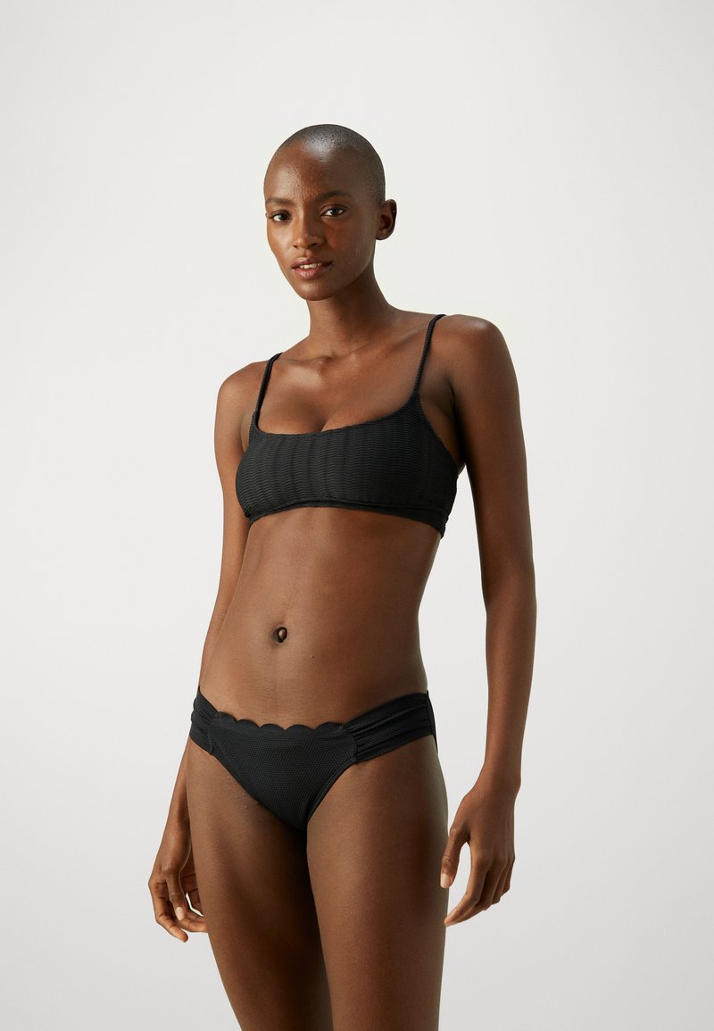 Čierny bikiny set s ryhovanou textúrou, tenkými ramienkami a vlnkovaným pásom na spodnej časti. Jednoduchý, elegantný dizajn.