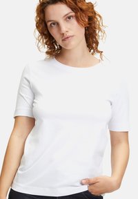 Biała koszulka z krótkim rękawem wykonana z gładkiej bawełny, z okrągłym dekoltem i luźnym fasonem, bez widocznych wzorów lub grafik.