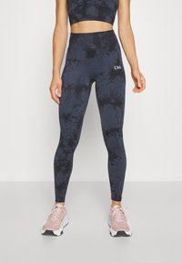 Leggings taille haute tie-dye bleu marine avec une finition texturée. Présente un logo sur le côté et associés à des chaussures de sport rose clair.