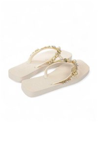 Beige teenslippers met gestructureerde zolen, voorzien van decoratieve gouden accenten, parels en schelpen op de band. Plat ontwerp, casual stijl.