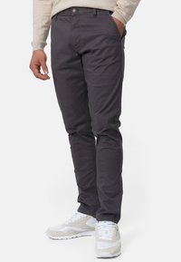 Ciemnoszare chinosy o slim fit, z zapięciem na guzik, przednimi kieszeniami i gładką fakturą materiału. Połączone z białymi sneakersami.
