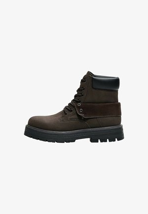 Stivaletto stringato marrone scuro con collo imbottito nero, spessa suola in gomma nera e dettaglio con risvolto ripiegato.