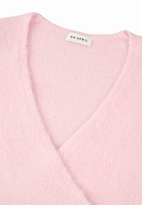 Rosa, weicher, gestrickter Pullover mit V-Ausschnitt. Der Stoff hat eine flauschige Textur und zeigt ein Etikett mit "OH APRIL" aufgestickt.