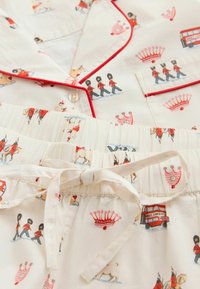 Set de pijamale albe cu bordură roșie, având imprimeuri cu gardieni londonezi, autobuze etajate, coroane și puguri, cu talie cu cordon la pantaloni.