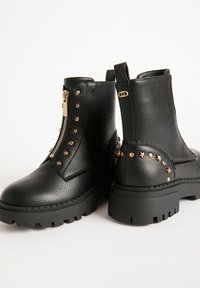 Botas de tobillo de piel negra con un acabado texturizado, que cuentan con un cierre lateral de cremallera, tachuelas en forma de estrella y una suela gruesa para una mejor tracción.