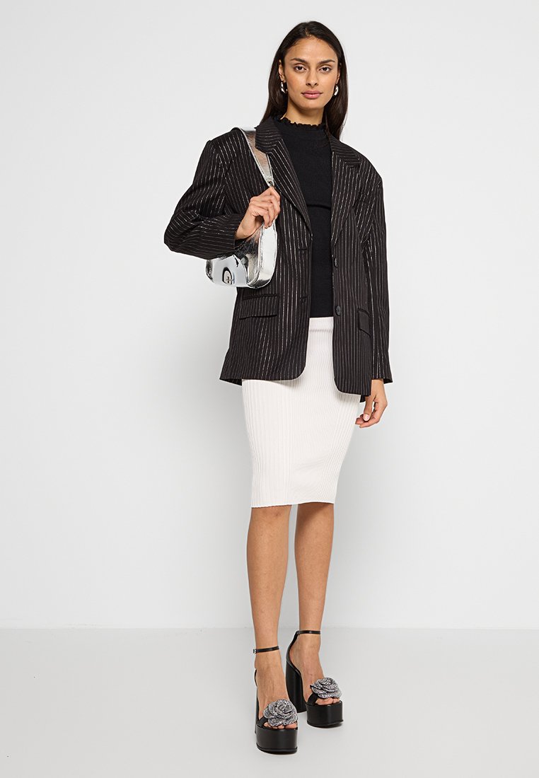 Czarna marynarka w prążki z dwoma przednimi kieszeniami, noszona na czarnym, teksturowanym topie, w połączeniu z białą, prążkowaną spódnicą midi oraz czarnymi, platformowymi szpilkami z kwiecistymi akcentami.