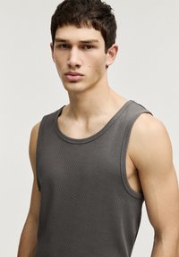 Débardeur gris à côtes avec de larges emmanchures et un col rond, présentant un tissu texturé et une coupe ajustée.