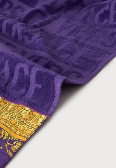Serviette violette avec texture de texte en relief et bordure décorative jaune et or à motifs sur un fond clair.