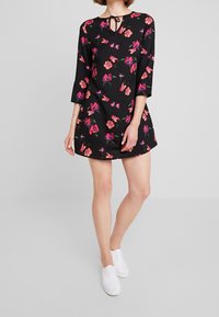 Schwarzes Blumenkleid mit runder Halslinie und Bindedetail, ausgestattet mit lebhaften rosa und lila Blumen, Dreiviertelärmeln und einer lockeren Passform.