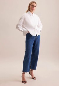 White oversized button-up shirt with a collar, paired with high-waisted blue straight-leg jeans and black strappy heels.