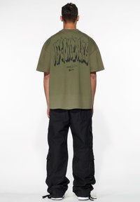Olive green oversized t-shirt with large black text on the back. Matched with black cargo pants featuring side pockets. Casual fit.