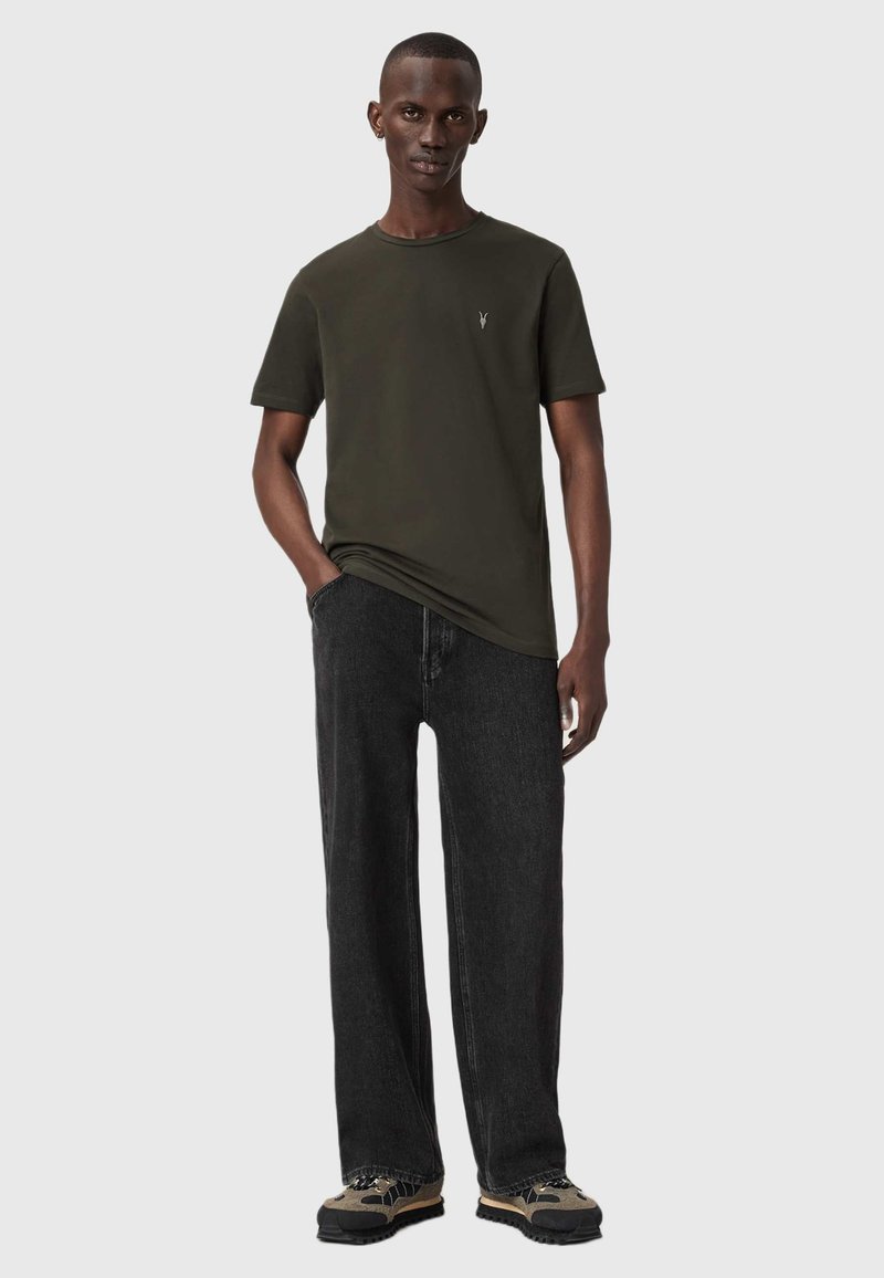 Tumma vihreä t-paita lyhyillä hihoilla, pyöreällä kaula-aukolla ja pienellä logolla. Yhdistetty löysiin mustiin farkkuihin ja teksturoituihin kenkiin.