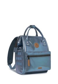 Metallisch blauer Rucksack mit strukturiertem Design, oberen Griffen, verstellbarem Gurt, vorderer Reißverschlusstasche und rundem Logo-Patch. Texturierte Oberfläche.