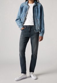 Ljusblå jeansjacka, vit t-shirt med rund hals, mörkgrå jeans och vita sneakers. Jackan har knappar och sidofickor.