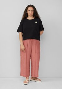 Schwarzes Baumwoll-T-Shirt mit einem kleinen weißen Sonnenmotiv, kombiniert mit lockeren, plissierten pinken Hosen und weißen Sandalen mit dicker Sohle.