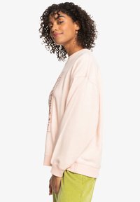 Lys rosa sweatshirt med avslappet passform, rund hals og grafisk trykk på forsiden. Teksturert stoff og overdimensjonerte ermer.