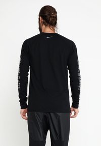 Schwarzes Longsleeve-Sportshirt mit grafischem Text auf beiden Ärmeln und einem kleinen Logo auf dem Rücken. Glattes Material, taillierter Schnitt.