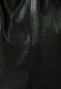 Svart lädermaterial med en texturerad yta. Har en subtil lyster, synlig sömmar längs kanten och en slät finish.