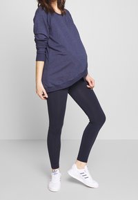 Sudadera de maternidad de manga larga en azul marino, con un ajuste holgado, combinada con leggins azul marino y zapatillas blancas, con tres franjas de colores.