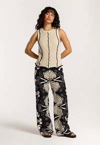 Bēša ribota tanktopiņa ar melnu volānu apdari, kopā ar vaļīgām melnām biksēm ar lieliem krēmkrāsas ziedu un dzīvnieku rakstiem. Melnas sandales.