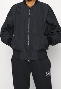 Black bomber jacket with zip closure, ribbed cuffs and hem, elasticated details on sleeves, front pocket, and lightweight fabric.