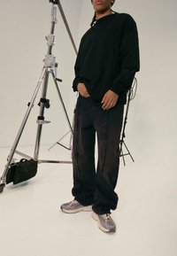 Black oversized sweatshirt with long sleeves paired with distressed black jeans. Footwear features gray sneakers with a textured design.