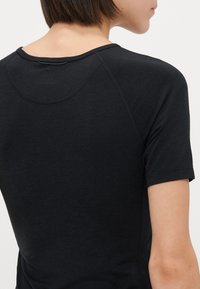 Zwarte T-shirt met korte mouwen, voorzien van een ronde halslijn en naadloos ontwerp. Glad materiaal met subtiele stiksels langs de schouders en de zoom.