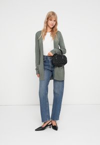 Cardigan verde deschis peste un top alb, cu blugi albastri cu talie inalta si pantofi cu varf ascutit negri. Geanta texturata neagra cu manere scurte.