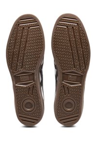 Brązowe gumowe podeszwy sneakersów z wzorem trzymania, z rowkami i okrągłymi akcentami. Czarne paski po bokach wskazują markę.