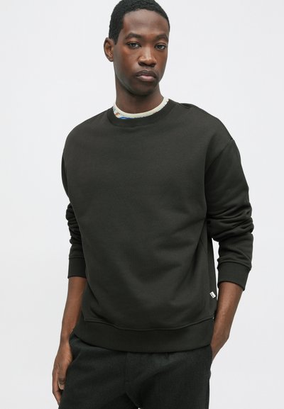 Ciemnozielona bluza z okrągłym dekoltem i ściągaczami przy mankietach. Wykonana z miękkiego materiału, posiada małą metkę z logo na dolnej lewej stronie.