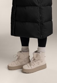 Beige ankelstövlar med tjock sula, gjorda av mjukt mocka, med snörning och ett varmt innerfoder. Matchas med ribbade yllestrumpor och svarta leggings.