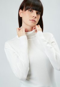 Weißer Rollkragenpullover aus weichem, strukturiertem Stoff. Verfügt über einen gerippten Kragen und Manschetten, mit einer taillierten Passform und langen Ärmeln.