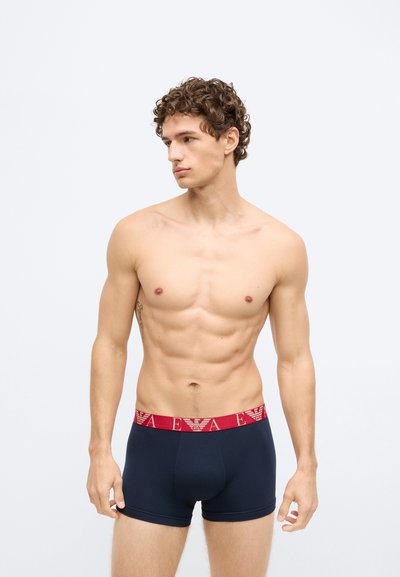 Cuecas boxer azul marinho com cintura elástica vermelha apresentando um padrão de logótipo. Tecido macio e elástico com design ajustado para conforto e suporte.