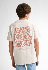 Beige katoenen T-shirt met een grote roze bloemenafdruk op de achterkant, korte mouwen en een ronde hals. Casual pasvorm met schone stiksels.