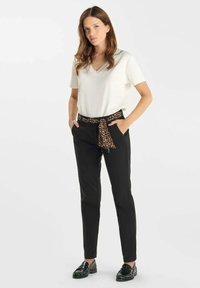 Vit V-ringad t-shirt i kombination med svarta byxor med ett leopardmönstrat bälte i midjan, kompletterat med svarta loafers.