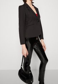 Svart kavaj med en enda knapp, figursydd design och avslappnade slag, kombinerad med blanka svarta leggings och en liten svart handväska.