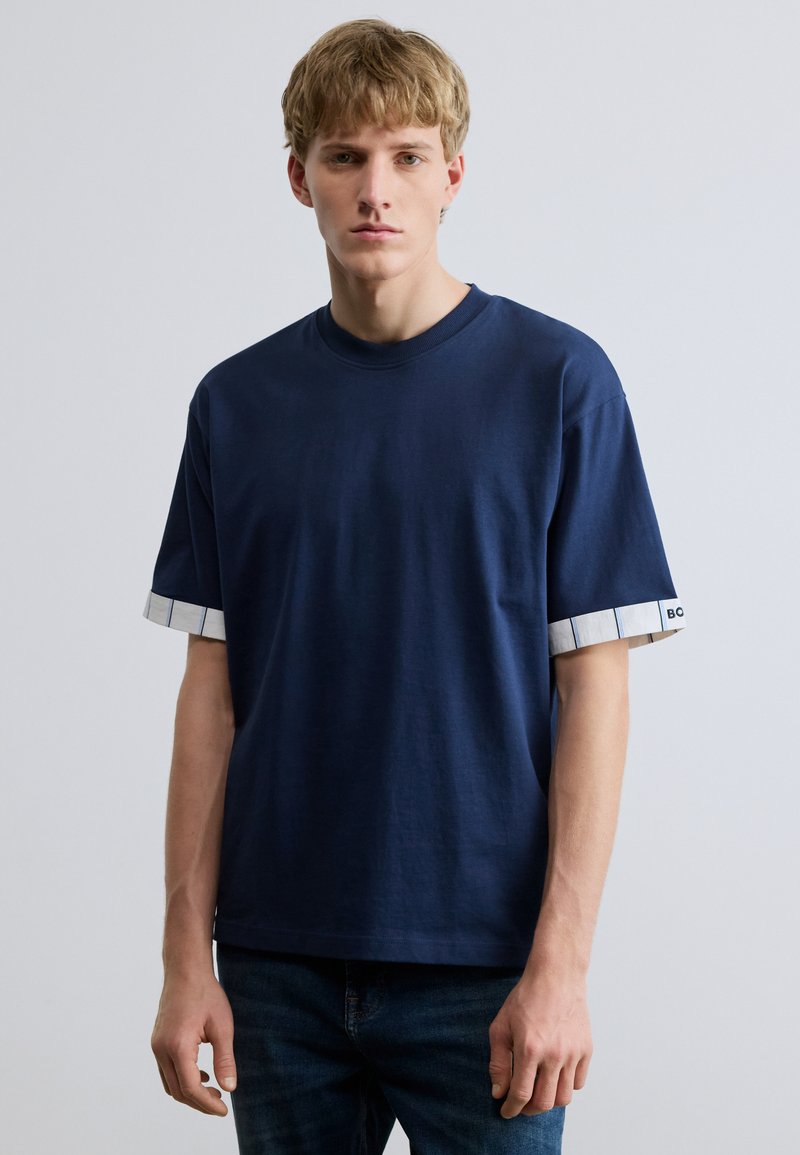 Tmavomodré bavlnené tričko s krátkymi rukávmi a vzorovaným bielo-modrým lemom. Jednoduchý okrúhly výstrih a voľný strih.