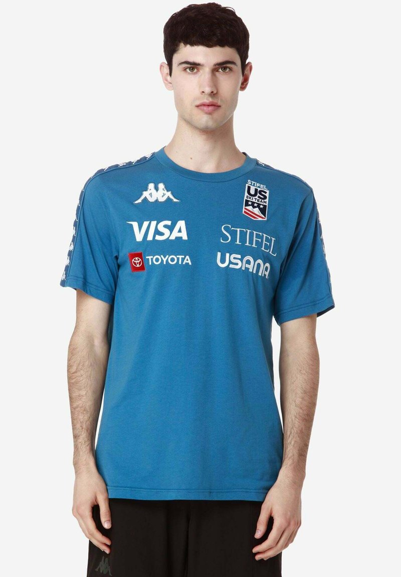 Maglietta sportiva blu realizzata in tessuto con maniche corte, che presenta diversi logo bianchi e rossi sul davanti e sulle maniche.