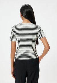Top de manga corta a rayas en blanco y negro, con un escote redondo y una silueta ajustada. El material parece suave con un acabado texturizado.