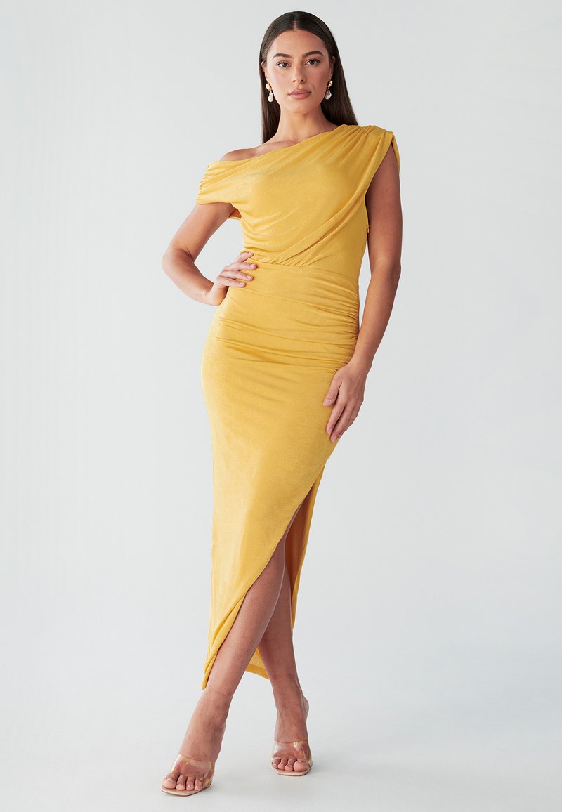 Robe jaune asymétrique avec tissu drapé, silhouette ajustée, fente latérale et longueur mi-mollet. Texture lisse et design décolleté épaules dénudées.